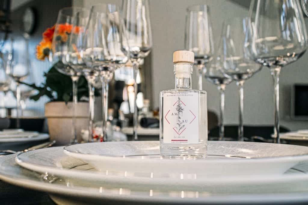 Miniflesje op bord met gepersonaliseerd label. Op de achtergrond een mooi gedekte tafel