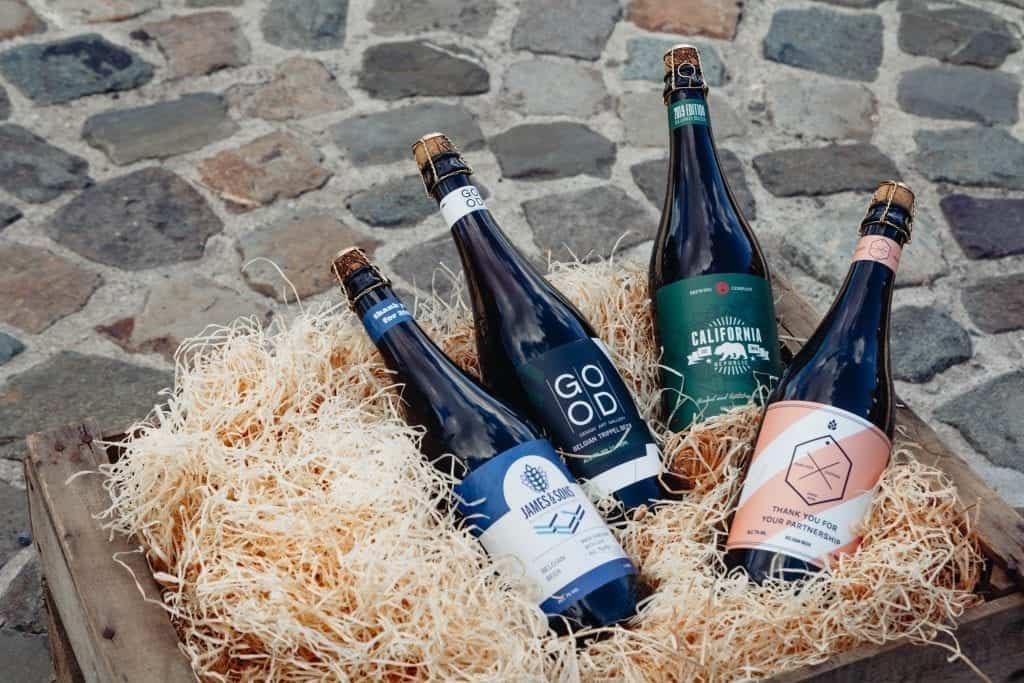 4 verschillende flessen bier met gepersonaliseerde labelen in een kratje hooi
