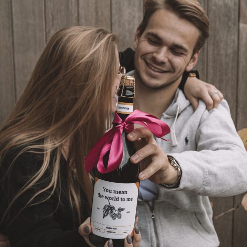 Omhelsend koppel met gepersonaliseerde bierfles als valentijnscadeau